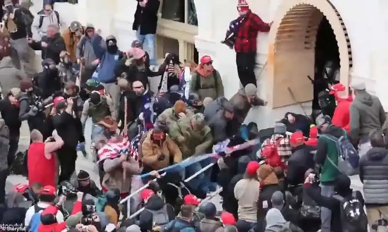 manifestanti picchiano un poliziotto con una bandiera americana a washington 