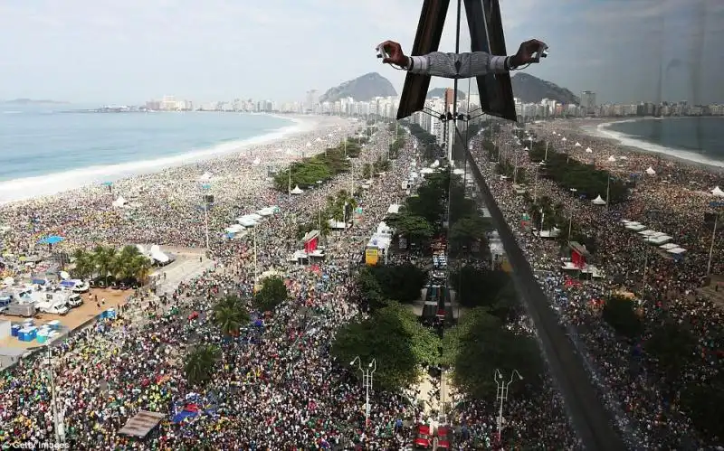 LA MANO DI UN UOMO SPUNTA DALLA FINESTRA DI UN HOTEL PER FOTOGRAFARE LA SPIAGGIA DI COPACABANA AFFOLLATA DAI PELLEGRINI 