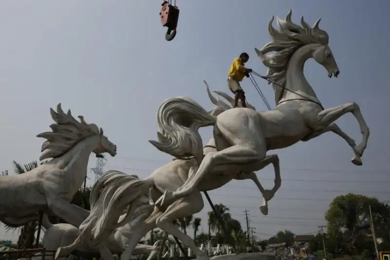 UN OPERAIO TIRA UNA CORDA IN CIMA ALLA STATUA DI UN CAVALLO IN INDONESIA 