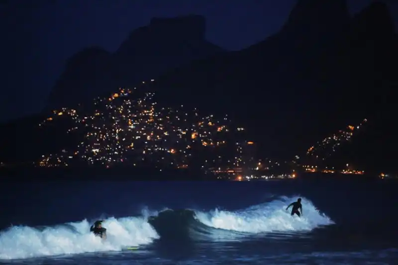 Surfisti cavalcano le onde con le favelas sullo sfondo a Rio de Janeiro in Brasile 