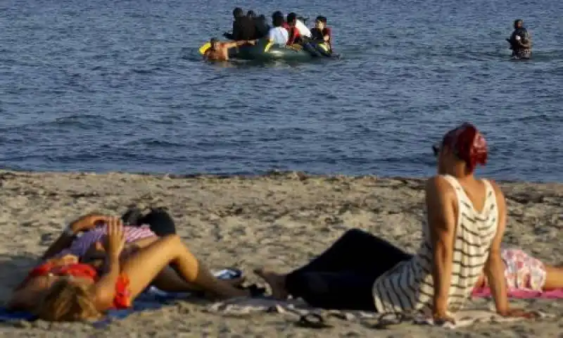 yannis behrakis turisti su una spiaggia mentre arriva un gommone di migranti in turchia