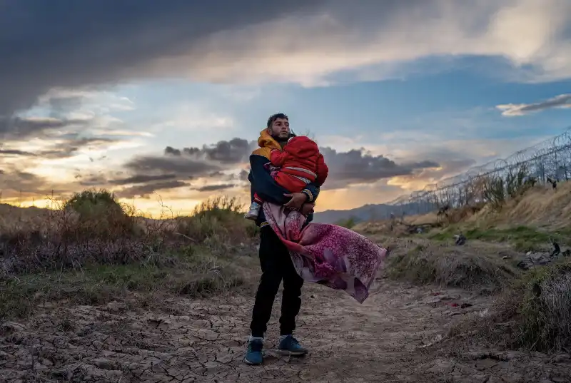 un uomo porta in braccio la figlia al confine messico usa   ph brandon bell